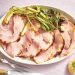 Sliced glazed ham served on a platter with roasted green onions and carving utensils nearby.