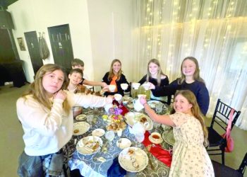 Children raise teacups together around a decorated table during an afternoon tea gathering.