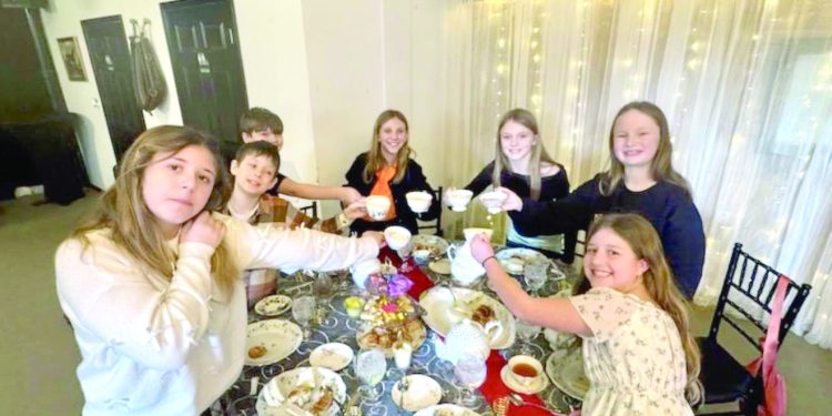 Children raise teacups together around a decorated table during an afternoon tea gathering.