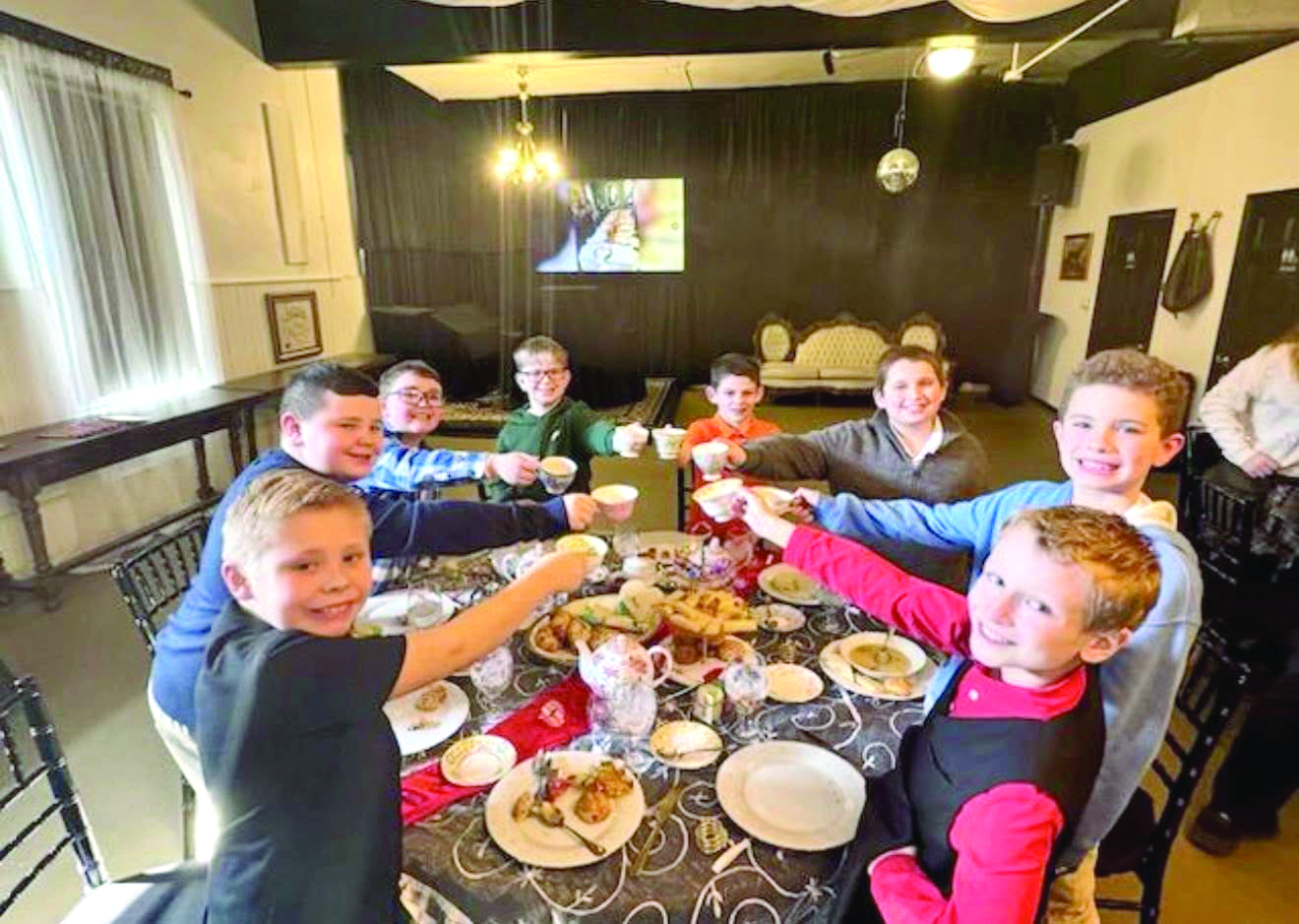 Young boys raise teacups together around a table during an afternoon tea gathering.