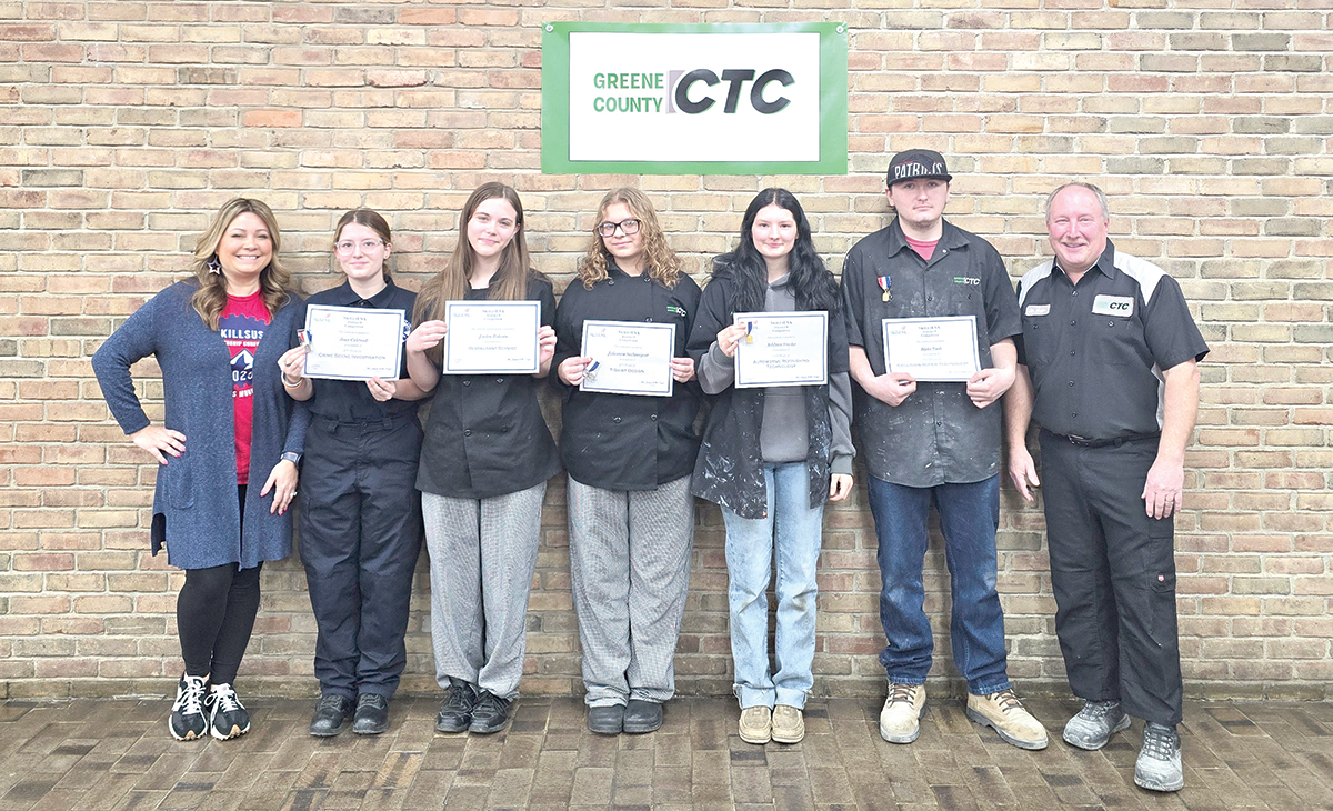 Greene County CTC students hold certificates while posing with instructors in front of a brick wall sign.