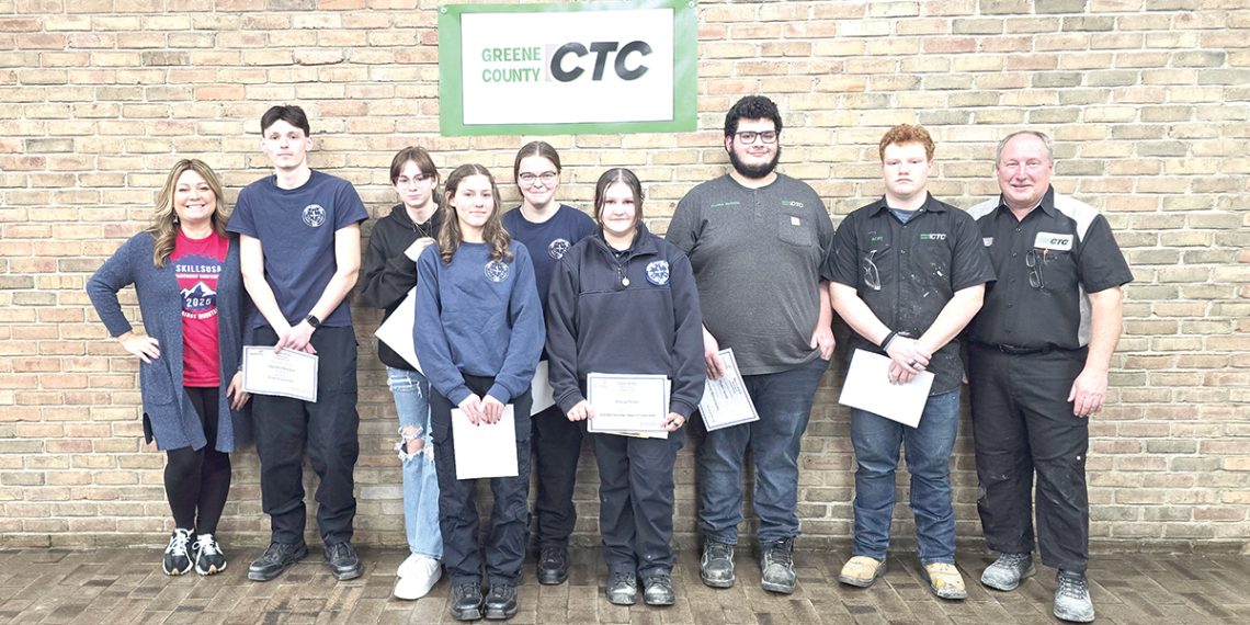 Students and instructors at Greene County CTC pose with certificates in front of a brick wall sign.