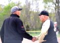 Two baseball coaches shake hands on the field during a game.