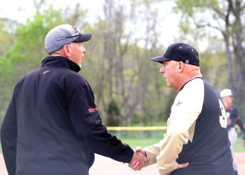 Two baseball coaches shake hands on the field during a game.