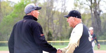 Two baseball coaches shake hands on the field during a game.