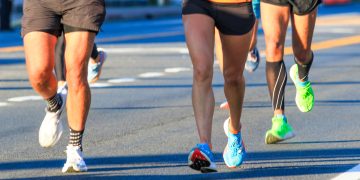 Close-up of runners’ legs and colorful shoes moving along a road during a race.