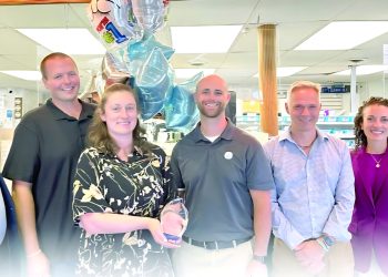 Group of pharmacy staff posing with an award and balloons inside a retail pharmacy.