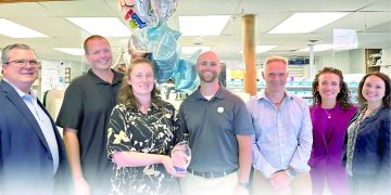 Group of pharmacy staff posing with an award and balloons inside a retail pharmacy.