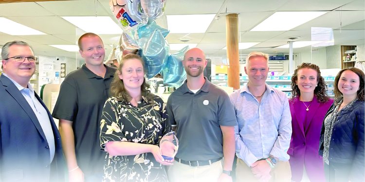 Group of pharmacy staff posing with an award and balloons inside a retail pharmacy.
