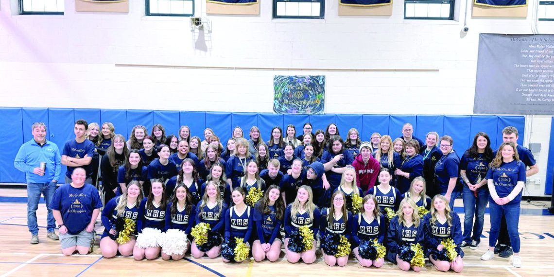 Students, staff, and cheerleaders pose together in a gym during a McOlympics event group photo.