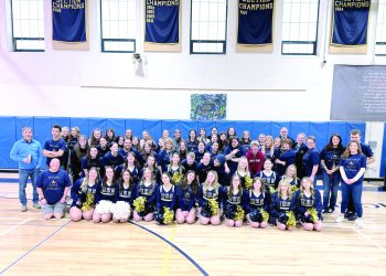 Students, staff, and cheerleaders pose together in a gym during a McOlympics event group photo.