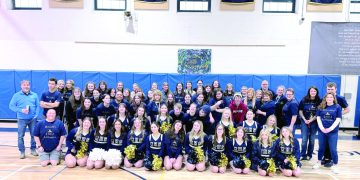 Students, staff, and cheerleaders pose together in a gym during a McOlympics event group photo.