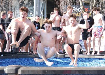 Students jump into a cold pool during a Polar Plunge event while others watch and cheer.
