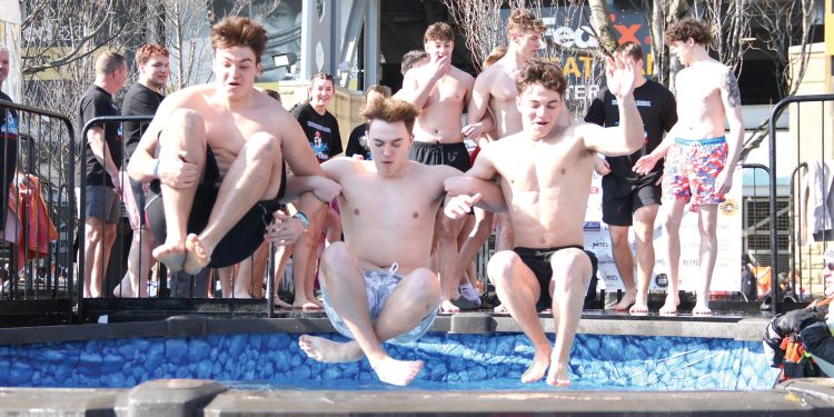 Students jump into a cold pool during a Polar Plunge event while others watch and cheer.