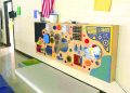 Colorful sensory activity board with interactive elements mounted on a school hallway wall.