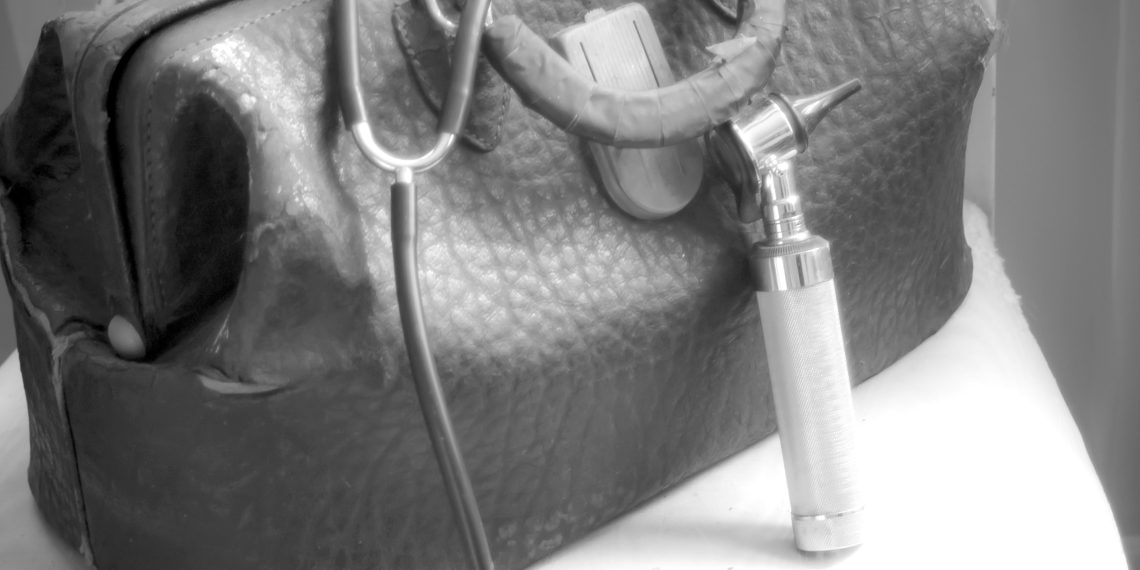 A worn old fashioned or vintage doctor's bag, stethoscope and otoscope on a worn chair.