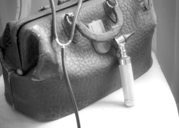 A worn old fashioned or vintage doctor's bag, stethoscope and otoscope on a worn chair.