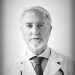 Black and white portrait of an older doctor wearing a white coat and looking at the camera.
