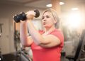 Woman lifting dumbbells during a strength training workout in a gym.
