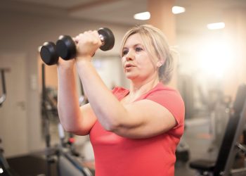 Woman lifting dumbbells during a strength training workout in a gym.
