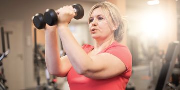 Woman lifting dumbbells during a strength training workout in a gym.