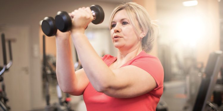 Woman lifting dumbbells during a strength training workout in a gym.