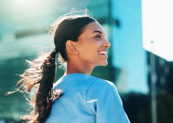 Smiling woman with a ponytail looking back outdoors with city buildings in the background.