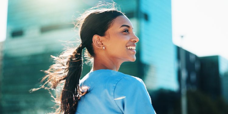 Smiling woman with a ponytail looking back outdoors with city buildings in the background.
