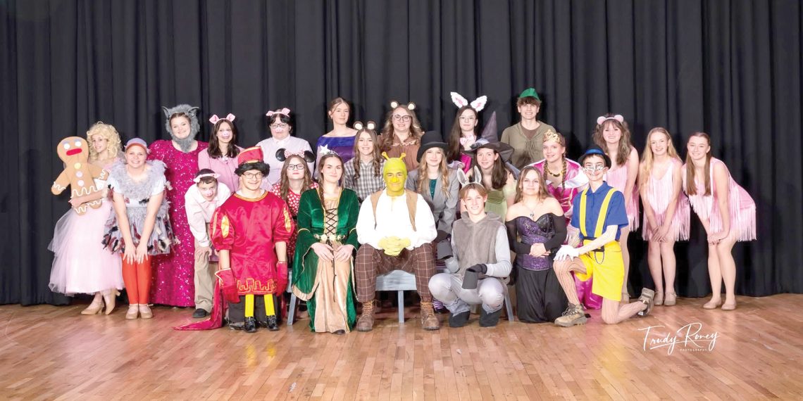 A group of students in costume pose together on a stage as a cast from a school play.