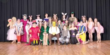 A group of students in costume pose together on a stage as a cast from a school play.