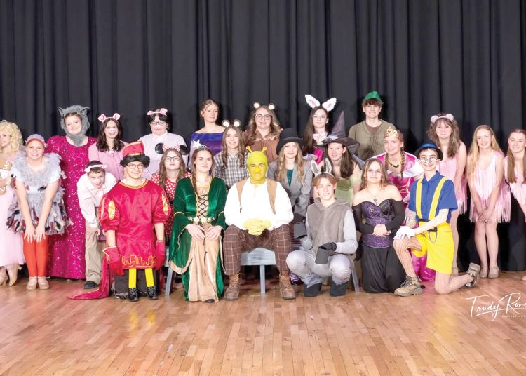 A group of students in costume pose together on a stage as a cast from a school play.