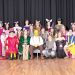 A group of students in costume pose together on a stage as a cast from a school play.