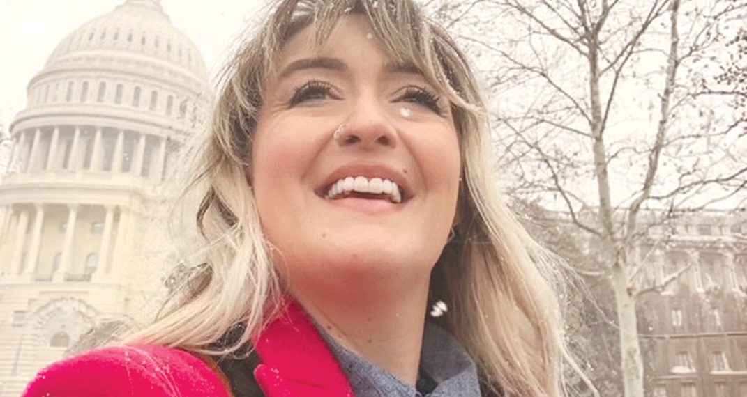 Woman in a red coat smiling in the snow with the US Capitol building in the background.