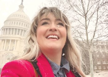Woman in a red coat smiling in the snow with the US Capitol building in the background.