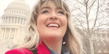 Woman in a red coat smiling in the snow with the US Capitol building in the background.