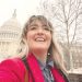 Woman in a red coat smiling in the snow with the US Capitol building in the background.