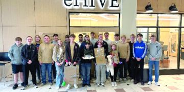 A group of students pose indoors in front of an eHIVE sign holding project displays from a school design activity.