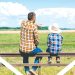 A man and child sit on a fence overlooking a farm field as the man points into the distance.