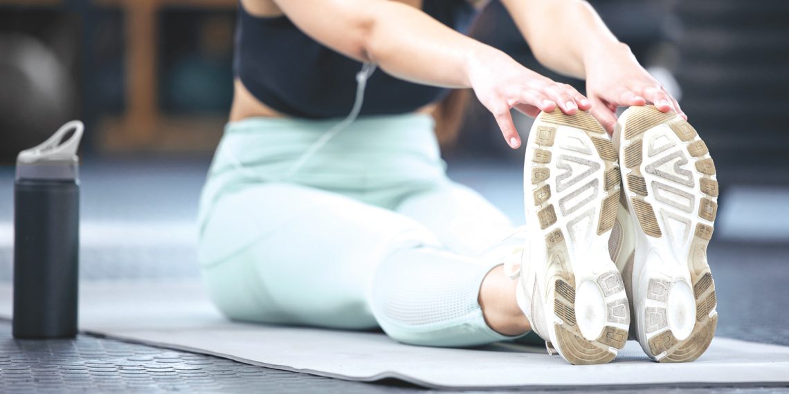 Person stretching forward to touch their toes on a mat with a water bottle nearby.