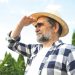 Man in a straw hat shades his eyes while looking into the distance outdoors.