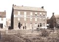A historic black and white photo shows the Rogers’ Photograph Rooms building with people and a horse-drawn wagon outside.