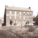 A historic black and white photo shows the Rogers’ Photograph Rooms building with people and a horse-drawn wagon outside.
