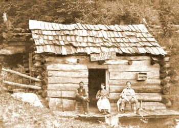A sepia historic photo shows three people sitting outside a rustic log cabin with a sign reading “Allums Resort 1887.”