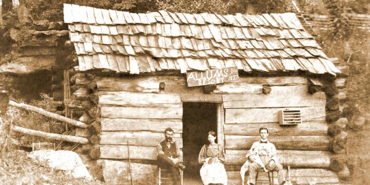 A sepia historic photo shows three people sitting outside a rustic log cabin with a sign reading “Allums Resort 1887.”