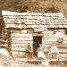 A sepia historic photo shows three people sitting outside a rustic log cabin with a sign reading “Allums Resort 1887.”