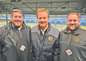 Three men wearing Pittsburgh Steelers apparel pose together inside a stadium media area overlooking the field.
