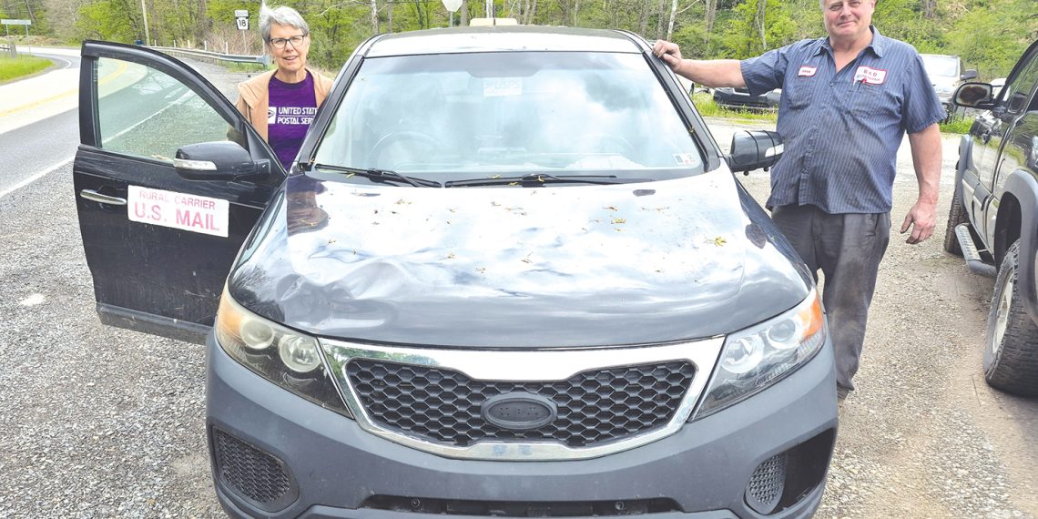 A retired rural mail carrier and mechanic pose beside a Kia Sorento used for mail delivery in Greene County.