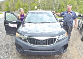 A retired rural mail carrier and mechanic pose beside a Kia Sorento used for mail delivery in Greene County.