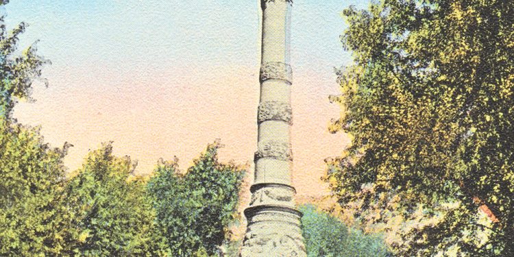 A tall stone monument with a statue on top stands in a tree-lined park under a blue sky.