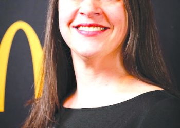 A smiling woman with long dark hair poses for a professional portrait against a black and gold background.